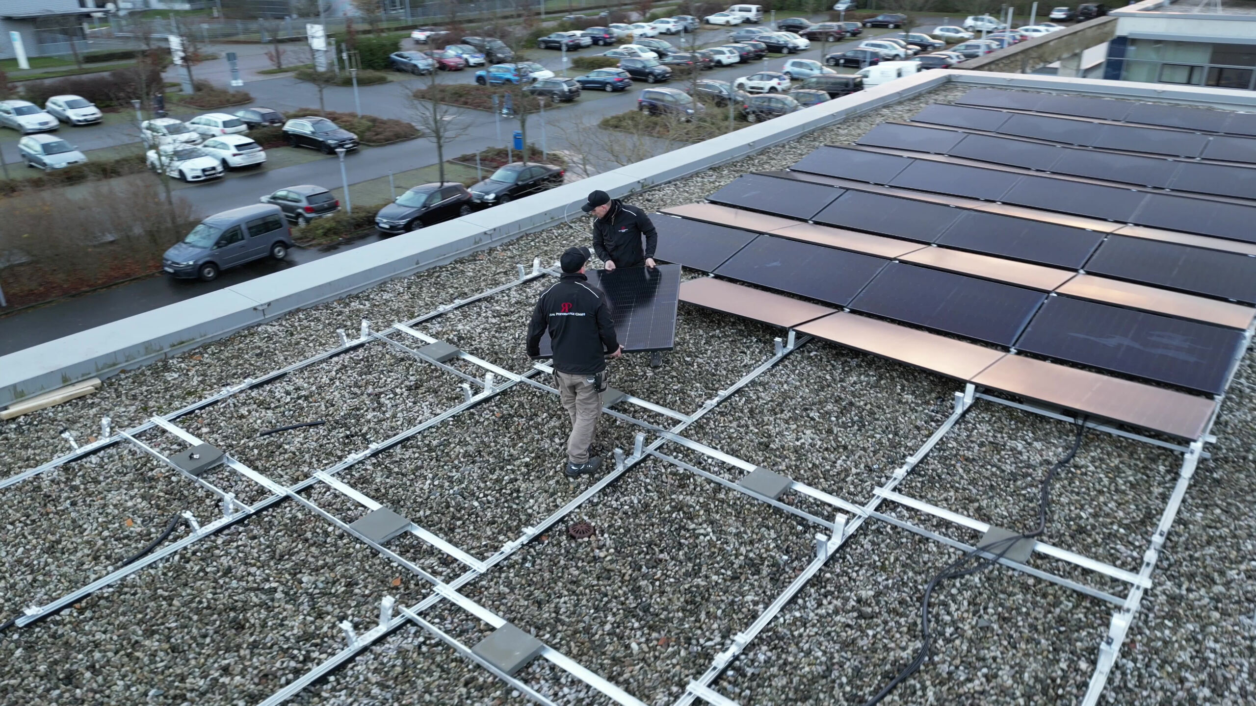 Zwei RP-Monteure tragen ein Solarmodul über ein Gewerbe-Flachdach, daneben fertige Modulreihen